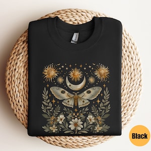 Pode incluir: Camisola preta com uma estampa gr&aacute;fica de uma mariposa com as asas abertas, cercada por estrelas, luas e flores. O design &eacute; em tons de dourado e branco.
