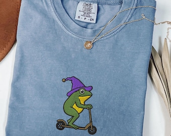 気まぐれな魔法使いのカエルの刺繍入りコンフォートカラーズ®Tシャツ、面白いスクーターのカエルのTシャツ、ウィアードコアの美的シャツ、カエルのウィッチコアギフト、カエルギフト