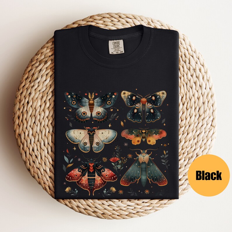 Puede incluir: Camiseta negra con un gr&aacute;fico de seis polillas coloridas con detalles intrincados sobre un fondo oscuro. Las polillas est&aacute;n dispuestas en un patr&oacute;n sim&eacute;trico con flores y estrellas que las rodean.