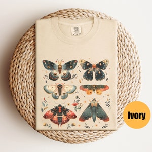 Puede incluir: Una camiseta beige con un estampado de seis polillas coloridas con detalles intrincados. Las polillas est&aacute;n rodeadas de peque&ntilde;as flores y hojas. La camiseta est&aacute; hecha de un material suave y c&oacute;modo, perfecta para el uso diario.