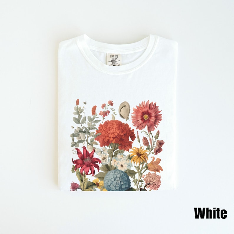 Pu&ograve; includere: Maglietta bianca con stampa floreale che presenta una variet&agrave; di fiori in tonalit&agrave; di rosso, rosa, arancio, giallo e blu. I fiori sono disposti in un design a bouquet e sono posizionati su uno sfondo bianco.