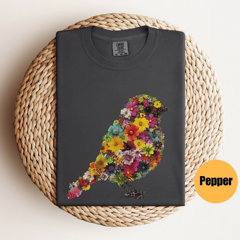May include: A dark gray t-shirt with a floral bird design. The bird is made up of colorful flowers and is outlined in black. The shirt has a crew neck and short sleeves.