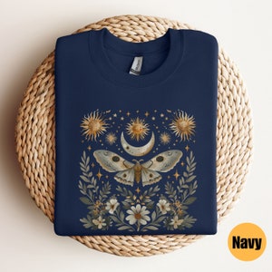 Pode incluir: Camisola azul marinho com um design de lua, estrelas e mariposa. A mariposa est&aacute; rodeada de flores e folhas. O design &eacute; em ouro e branco.