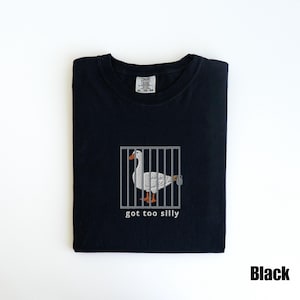 May include: Black t-shirt featuring a white goose inside a gray cage with the text "got too silly" below the cage. The goose has orange feet and a gray beak. The shirt has a Comfort Colors tag.