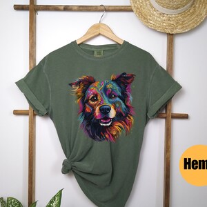 May include: A green t-shirt featuring a colourful graphic of a dog's face. The dog has a black nose and brown eyes. The t-shirt is made from hemp.