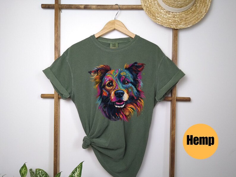 May include: A green t-shirt featuring a colourful graphic of a dog's face. The dog has a black nose and brown eyes. The t-shirt is made from hemp.