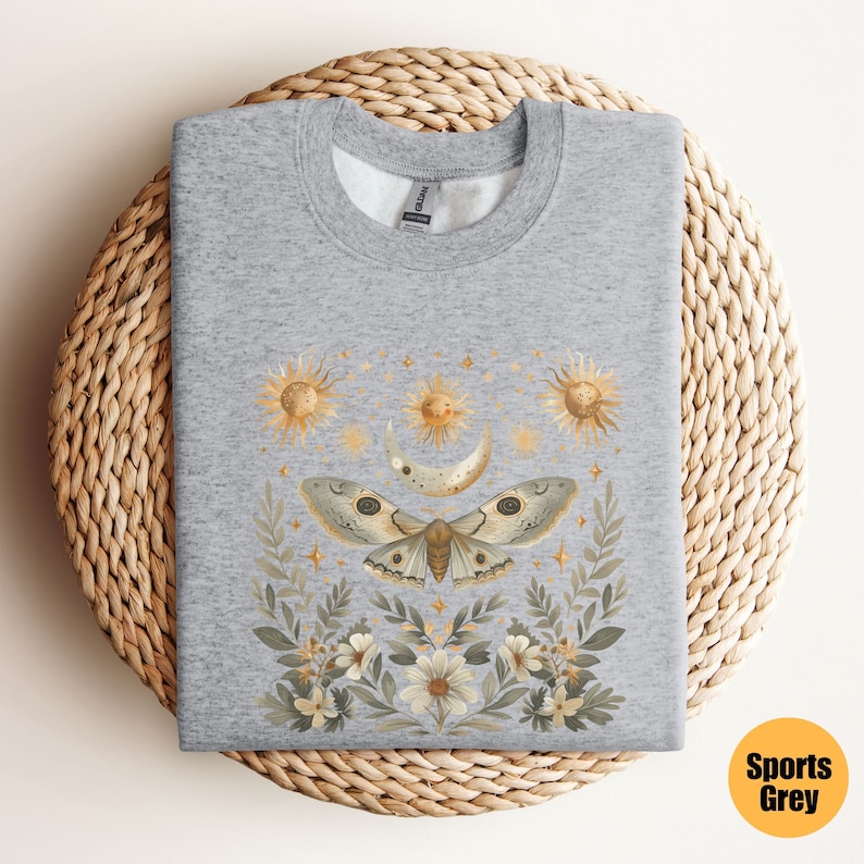 Pode incluir: Uma camisa de moletom cinza com uma estampa de uma mariposa, lua e s&oacute;is cercados por flores e estrelas. A estampa &eacute; em tons de dourado, marrom e branco.