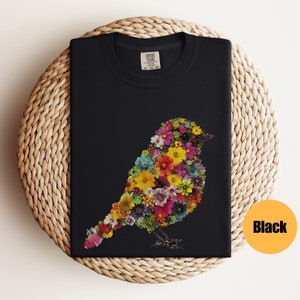 May include: Black t-shirt with a colorful bird design made of flowers. The bird is facing right and has a long tail. The shirt is made of a soft, comfortable material.