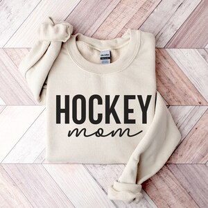 May include: A beige sweatshirt with the text "HOCKEY mom" printed in black.