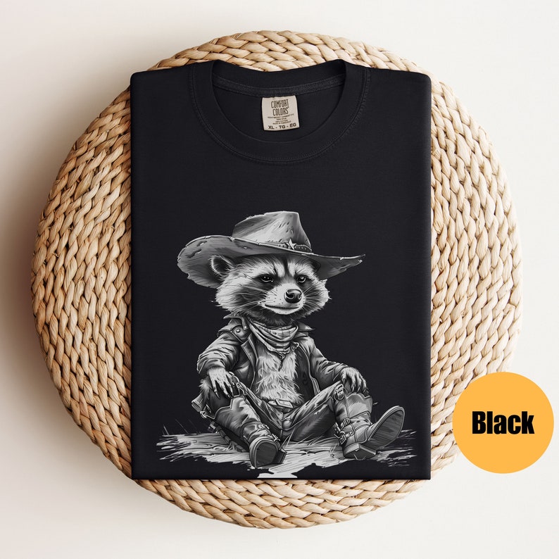 May include: Black t-shirt with a graphic of a raccoon wearing a cowboy hat and leather jacket. The raccoon is sitting with its legs crossed and wearing cowboy boots.