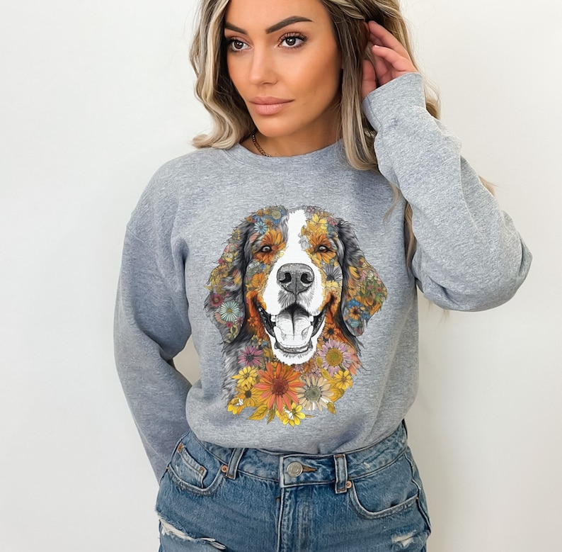 K&ouml;nnte beinhalten: Ein graues Sweatshirt mit einem floralen Design eines Berner Sennenhunds. Das Fell des Hundes besteht aus bunten Blumen und der Hintergrund ist einfarbig grau.
