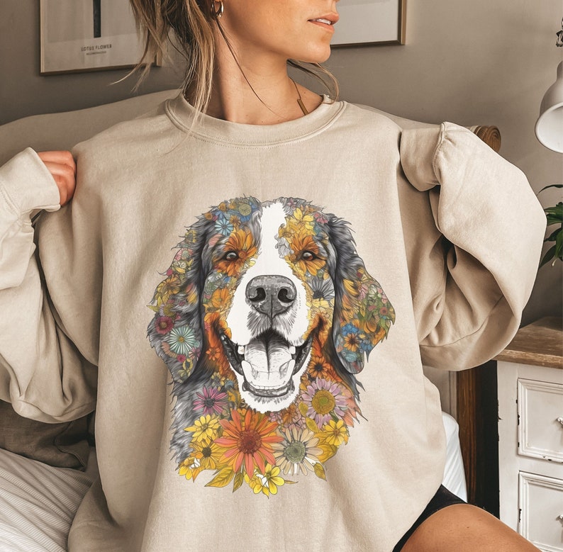 K&ouml;nnte beinhalten: Ein beiger Pullover mit einem floralen Design eines Berner Sennenhunds. Das Fell des Hundes besteht aus bunten Blumen.