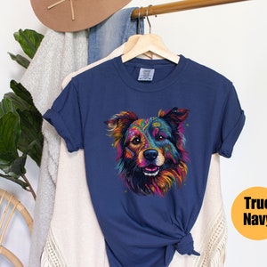 May include: A navy blue t-shirt featuring a colourful, psychedelic dog illustration. The dog has a black nose and brown eyes. The text "True Navy" is in a yellow circle on the right side of the image.
