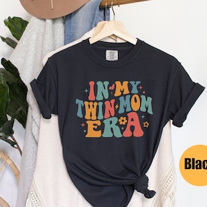 Może przedstawiać: Czarny T-shirt z napisem "In My Twin Mom Era" w kolorowych, retro literach.