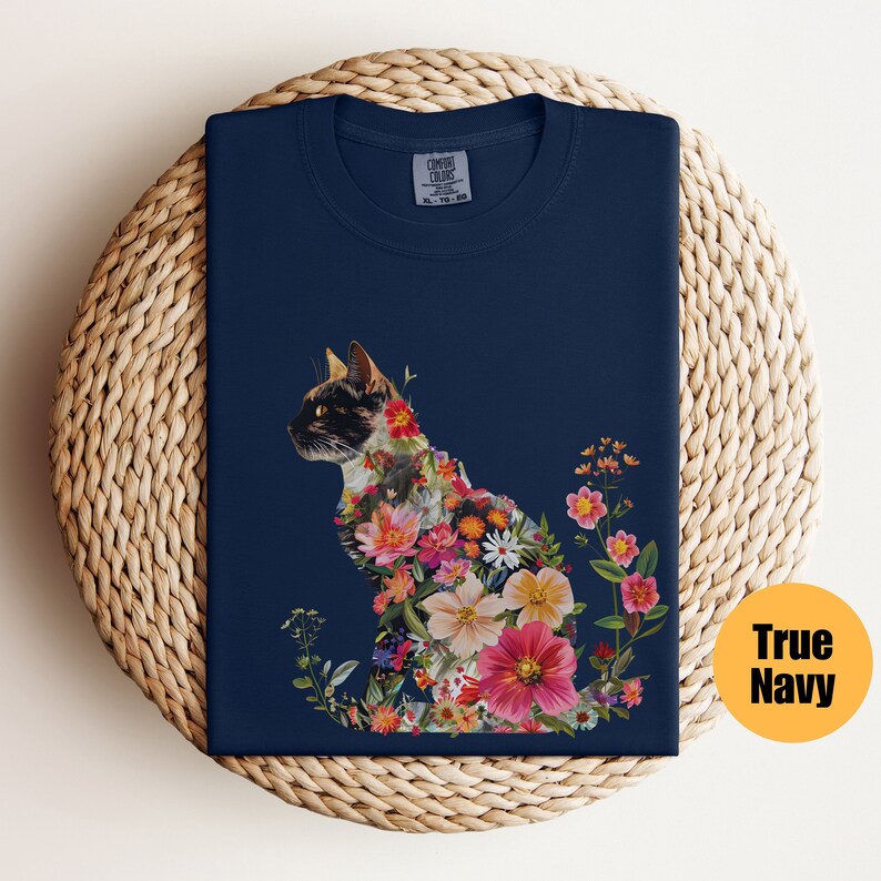 May include: A navy blue t-shirt featuring a floral cat design. The cat is made up of colourful flowers and leaves. The shirt has a crew neck and short sleeves.