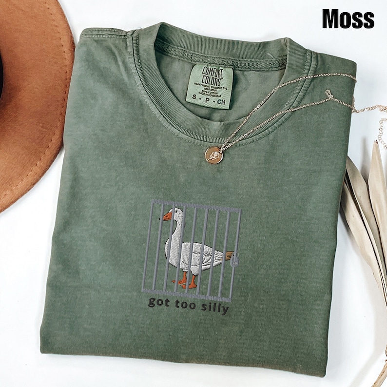 May include: A green t-shirt with a white duck in a cage and the text "got too silly".