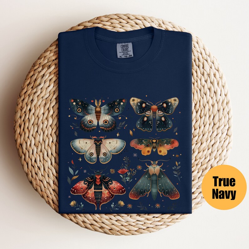 Puede incluir: Una camiseta azul marino con un dise&ntilde;o de seis polillas coloridas con detalles intrincados. Las polillas est&aacute;n dispuestas en una cuadr&iacute;cula en la parte delantera de la camiseta. La camiseta tiene cuello redondo y mangas cortas.