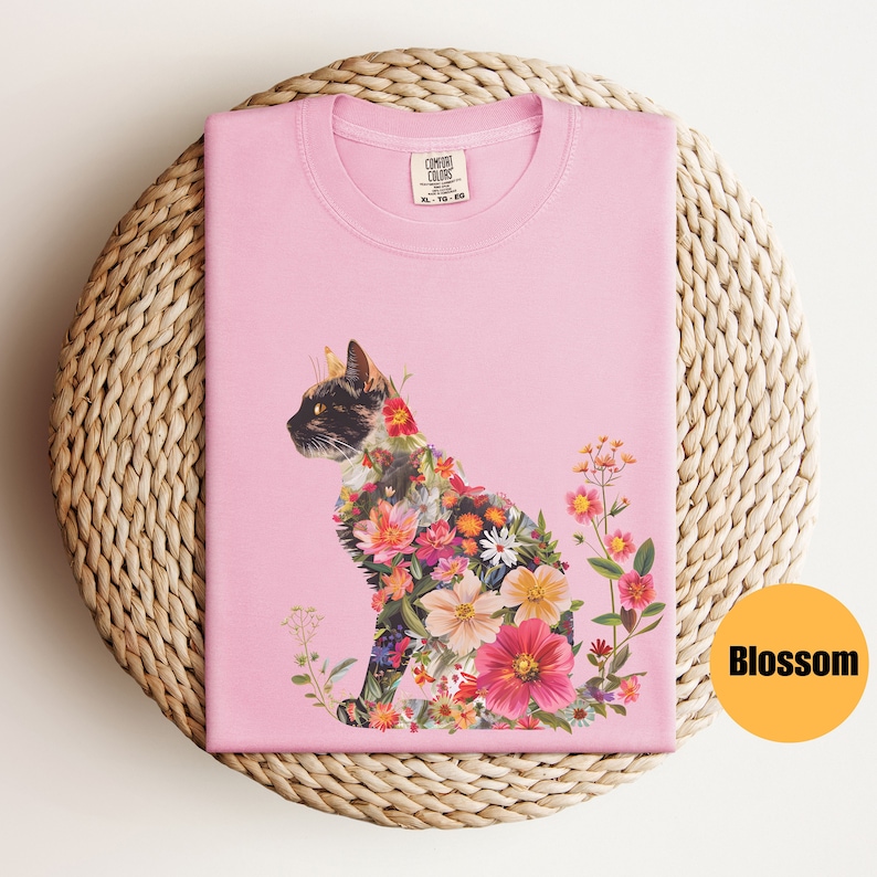 May include: Pink t-shirt featuring a floral cat design. The cat is made up of colourful flowers and leaves. The shirt has the text "COMFORT COLORS" on the tag.