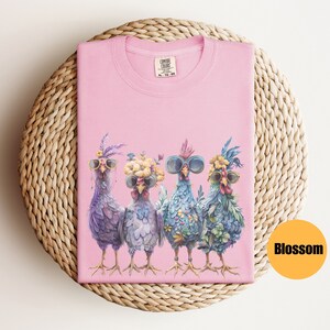 Peut inclure: T-shirt rose avec un motif de quatre poulets portant des lunettes de soleil et des bandeaux floraux. Les poulets sont debout en rang et le texte "COMFORT COLORS" est visible sur le t-shirt.
