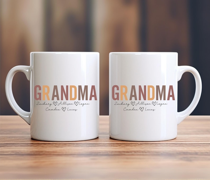 以下が含まれることがあります： ブラウン、オレンジ、ピンクの文字で「Grandma」と書かれた白いセラミック製のマグカップ2つ。マグカップには、「Zachary、Allison、Logan、Camden、Lucas」という名前が「Grandma」の下に書かれており、各名前の間にハートマークがあります。