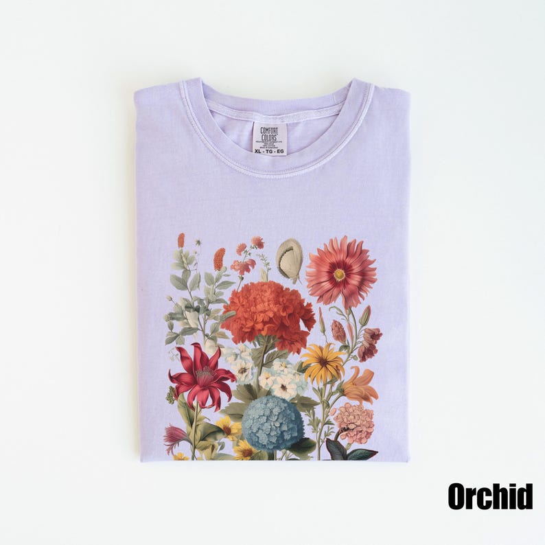 Pu&ograve; includere: Una t-shirt color lavanda con una stampa floreale che presenta una variet&agrave; di fiori in tonalit&agrave; di rosso, arancione, rosa, giallo e blu. La t-shirt ha un collo rotondo e maniche corte. Il testo "COMFORT COLORS" &egrave; visibile sull'etichetta.