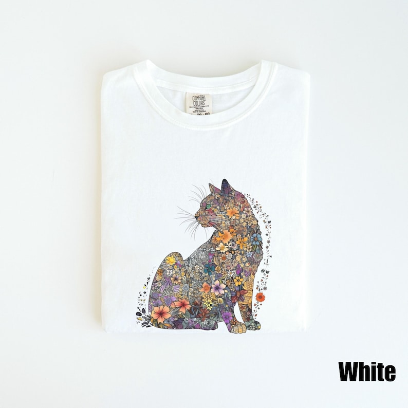 May include: White t-shirt with a floral cat design. The cat is made up of colorful flowers and leaves. The t-shirt has a crew neck and short sleeves.