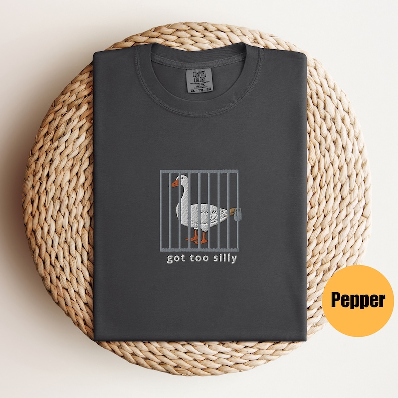 May include: A dark gray t-shirt with a white goose in a cage and the text "got too silly".