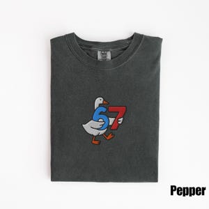 Peut inclure: T-shirt gris fonc&eacute; avec un motif brod&eacute; d'une oie portant les chiffres 6 et 7. L'oie est blanche avec les pieds et le bec orange. Les chiffres sont bleus et rouges. Le mot "Pepper" est dans le coin inf&eacute;rieur droit.
