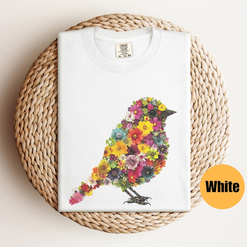 May include: White t-shirt with a floral bird design. The bird is made up of colorful flowers and is outlined in black. The shirt has a tag that says "Comfort Colors" on it.