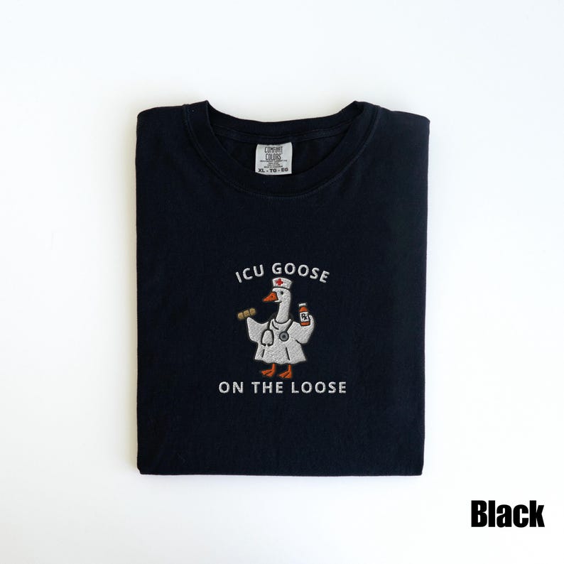 May include: Black t-shirt with the text "ICU GOOSE ON THE LOOSE" and a cartoon goose wearing a nurse's uniform. The goose is holding a stethoscope and a bottle of medicine. The shirt is folded neatly.