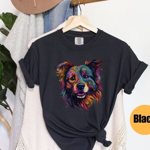 May include: A black t-shirt featuring a colourful graphic of a dog's face. The dog has a black, brown and white coat with colourful patterns on its fur. The dog is looking directly at the viewer.