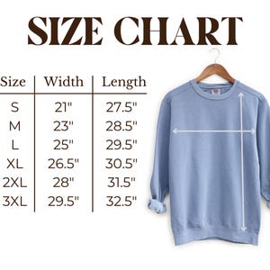 May include: A light blue sweatshirt hangs on a wooden hanger, with a size chart displayed to the left. The chart shows measurements for width and length in inches for sizes S through 3XL. The text "SIZE CHART" is at the top.