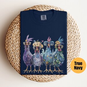 Peut inclure: Un t-shirt bleu marine avec un motif de quatre poulets portant des lunettes de soleil et des bandeaux floraux. Les poulets sont debout en rang et regardent le spectateur. Le t-shirt a une &eacute;tiquette qui dit "Comfort Colors" et "XL - 70/30"