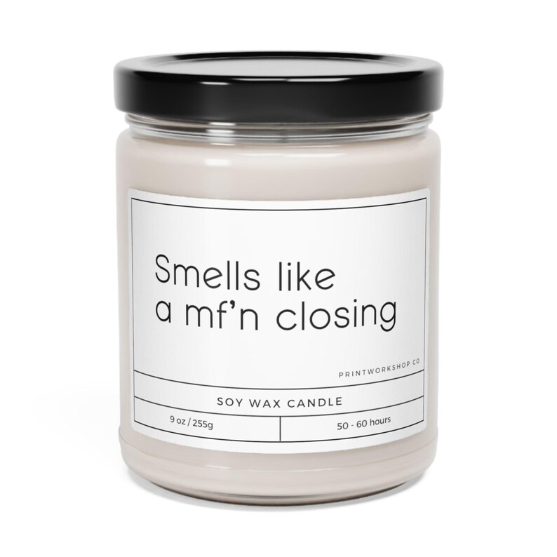 May include: A beige glass candle jar with a black lid. The label reads "Smells like a mf'n closing" and "Soy Wax Candle". The candle is 9 oz / 255g and has a burn time of 50-60 hours.