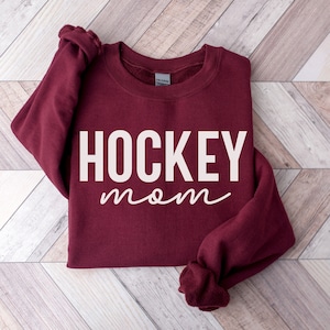 May include: Burgundy sweatshirt with the text "HOCKEY mom" in white and pink lettering.