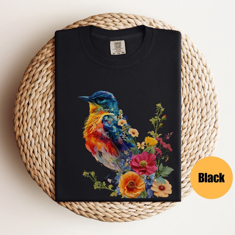 May include: A black t-shirt featuring a colourful bird and flowers printed on the front. The bird is a vibrant mix of blue, yellow, orange, and red. The flowers are a mix of pink, yellow, and blue.