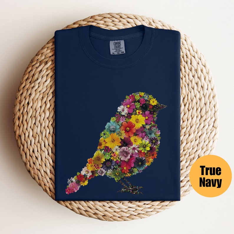 May include: A navy blue t-shirt with a floral bird design. The bird is made up of colorful flowers and is outlined in black. The shirt is made of a soft, comfortable material.