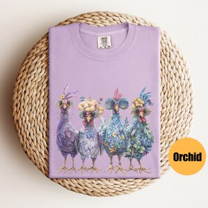 Peut inclure: Un t-shirt lavande avec un motif de quatre poulets portant des lunettes de soleil et des bandeaux floraux. Les poulets sont debout en rang et regardent le spectateur. Le texte "COMFORT COLORS" est visible sur l'&eacute;tiquette du t-shirt.