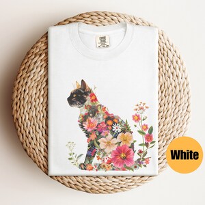 May include: White t-shirt featuring a floral cat design. The cat is made up of colourful flowers and is sitting in a profile pose. The background is white.