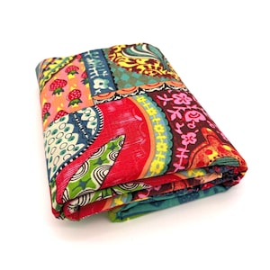 May include: A folded piece of fabric featuring a vibrant patchwork design with various patterns including red strawberries, yellow flowers, green geometric shapes, and blue paisley motifs in a multi-colored composition of red, pink, green, and blue.
