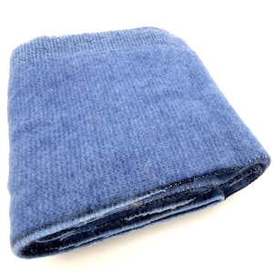 May include: A folded blue textile blanket with a textured, woven surface. The fabric features a consistent medium blue hue throughout, with a visible grid-like weave pattern and a slightly fuzzy, soft appearance across the entire surface area.