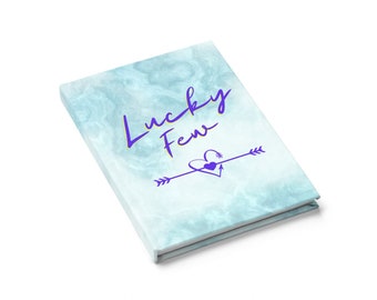 May include: A blue marble-patterned journal with the text "Lucky Few" in purple and yellow lettering. A purple heart with an arrow through it is centred below the text.