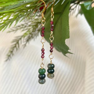 May include: Gold-toned dangle earrings with a combination of red and green beads. The earrings feature a series of small, round red beads and three stacked green beads. The earrings are suspended from gold-colored ear wires.