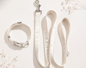 May include: A cream-colored pet collar and matching leash set. The collar features a plastic side-release buckle and a metal D-ring. The leash includes a silver-toned metal swivel snap hook at one end and a loop handle at the other end.