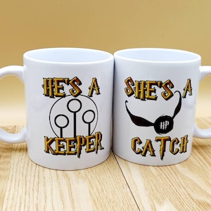 May include: Two white ceramic mugs with the text "HE'S A KEEPER" and "SHE'S A CATCH" in gold and black lettering. The "KEEPER" mug features a Quidditch goal post design, while the "CATCH" mug has a Snitch graphic.