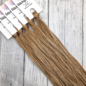 May include: Several skeins of hand-dyed Desert Camel embroidery floss. Each skein is 8 yards of 100% cotton thread, with a tan color. The floss is bundled with a white label that has the brand name and color information.