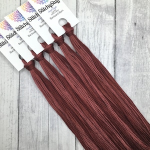 May include: Six skeins of hand-dyed 100% cotton embroidery floss in a deep reddish-brown color. The floss is labeled "StitchyStu" and "Backyard Barn".