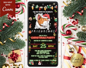 May include: A smartphone screen displays a Christmas party invitation with a cat wearing a Santa hat. The invitation reads "FRIENDSMAS" and includes party details. Festive decorations like candy canes, ornaments, and greenery surround the phone.