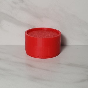 May include: A red, cylindrical, 3D printed object with a textured top.