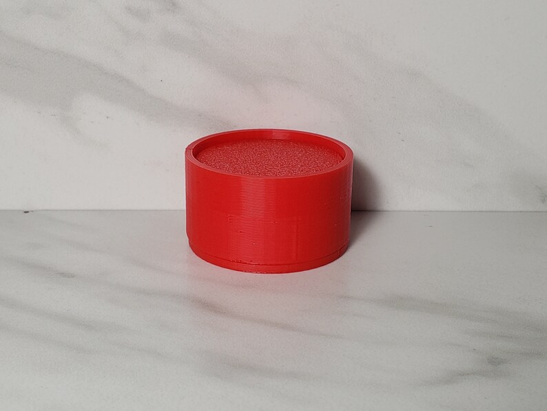 May include: A red, cylindrical, 3D printed object with a textured top.